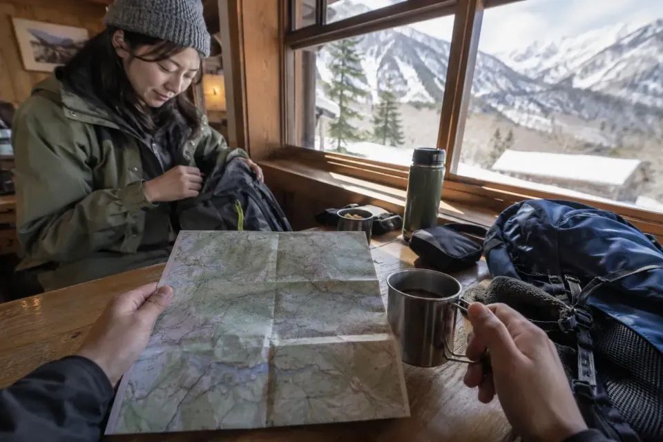 First-person preparation scene of organizing a backpack and winter jacket by the cabin window.