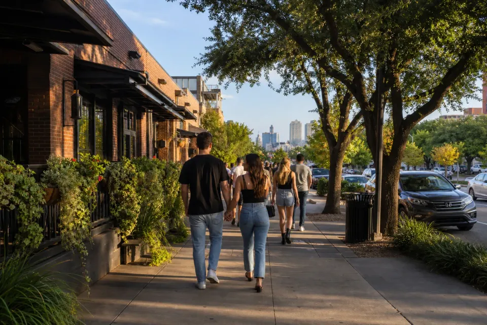 Travellers walking past shaded brick storefronts on Lower Greenville in Dallas in late afternoon